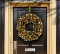 a christmas wreath on the front door of a house with lights hanging from it's side