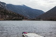 a wooden dock sitting in the middle of a lake surrounded by mountains and trees on a cloudy day