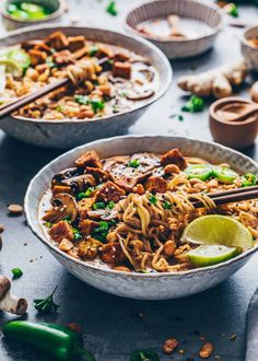 two bowls filled with noodles and vegetables next to some chopsticks on the table