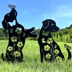 two metal dogs with butterflies on their backs in the grass, one is black and the other is white