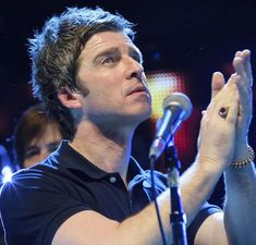 a man standing in front of a microphone holding his hands up to the side with both hands