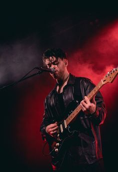 a man holding a guitar while standing in front of a microphone on top of a stage