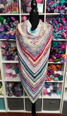 a multicolored triangle shawl is on display in front of many balls of yarn