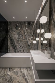 a bathroom with marble walls and flooring, lights hanging from the ceiling above the bathtub