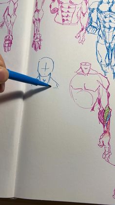 a hand is holding a pencil over an open book with drawings of different superheros