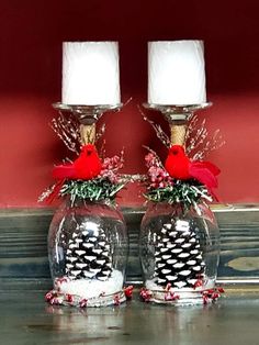 two clear glass vases with pine cones and red cardinal on them, sitting next to each other