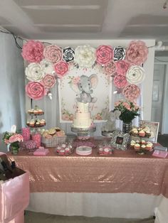 a table topped with lots of cakes and cupcakes next to a wall covered in paper flowers