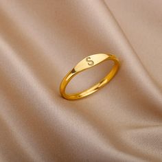 a gold ring with the letter s on it sitting on a satin surface in closeup