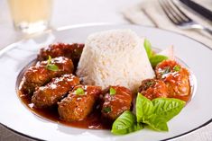 a white plate topped with meatballs covered in sauce and garnished with green leaves