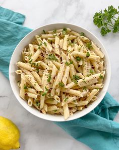 a white bowl filled with pasta and garnished with parsley next to a lemon