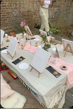 an outdoor table set up with easels and paintings on it for art enthusiasts to view