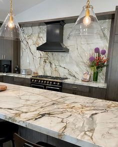 a kitchen with marble counter tops and two pendant lights hanging over the stove top oven