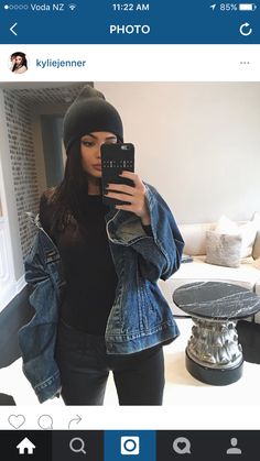 a woman taking a selfie in her living room wearing a denim jacket and beanie