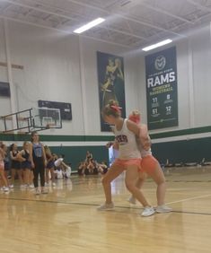 two women are wrestling in an indoor basketball court while people watch from the sidelines