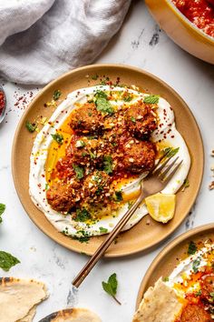 two plates with meatballs and sauce on them next to some pita breads