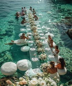 a long table is set up in the water with white flowers and plates on it