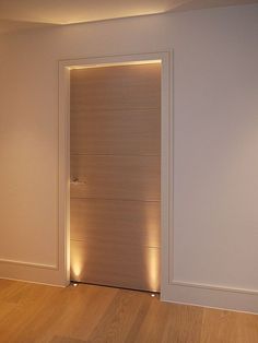 an empty room with a wooden door and light on the wall above it, along with hard wood flooring