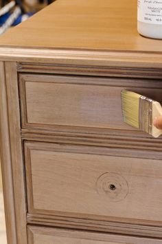 a paintbrush is being used to paint a wooden dresser with wood grained drawers