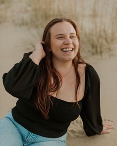 a woman sitting in the sand with her hands behind her head and smiling at the camera