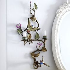 a wall mounted candle holder with flowers and birds on it next to a round mirror