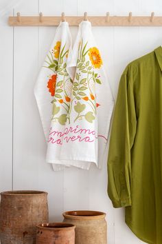 two tea towels hanging on a wooden rack next to pots and vases in front of a white wall