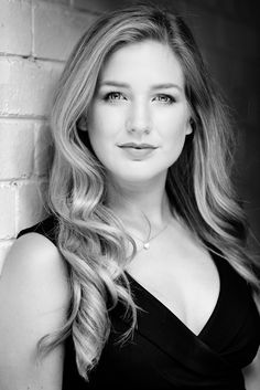 a woman with long blonde hair posing for a black and white photo in front of a brick wall