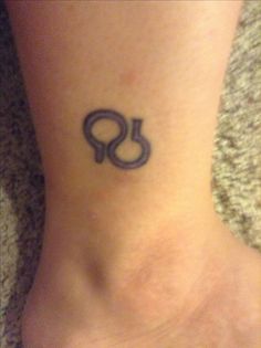 a small tattoo on the foot of a woman with an omen symbol in it