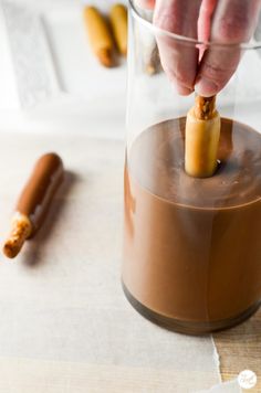 a person is dipping something into a glass with hot sauce and cinnamon sticks in it