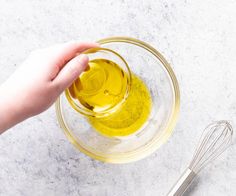 someone is mixing ingredients in a glass bowl with a whisk on the side