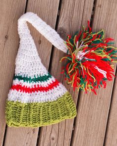 a crocheted hat with a pom - pom attached to it sitting on a wooden surface