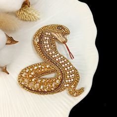 a gold and white snake brooch sitting on top of a white flower vase next to cotton