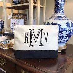 a blue and white vase sitting on top of a wooden table next to a monogrammed bag