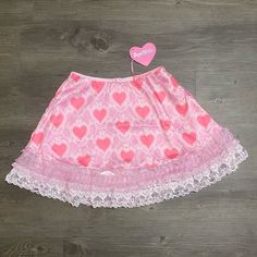 This Mini Skirt Has An All Over Hearts, Bows, And Pearls Graphic Print, A Lace And Ruffle Trim, A Low Waist Fit, And A Back Zip Closure. Cute Pleated Mini Skirt, Cute Mini Skort With Lined Skirt, Cute Mini Length Lined Skort, White Mini Skirt In Fairy Kei Style, Fairy Kei White Mini Skirt, White Fairy Kei Mini Skirt, Pink Mini Skirt With Lace Trim, Cute White Skirted Skort, Casual Pink Skirt With Lace Trim