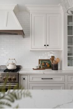 a kitchen with white cabinets and stainless steel stove top oven, range hood and tea kettle on the counter