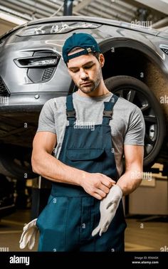 a man in overalls is working on the front wheel of a car with gloves