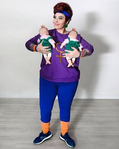 a woman holding two babies in her arms and wearing blue pants with an orange headband