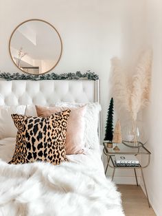 a white bed topped with lots of pillows next to a night stand and christmas trees