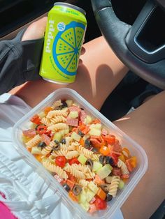 a plastic container filled with pasta salad next to a can of soda