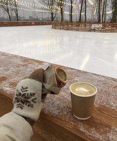 a cup of coffee sitting on top of a wooden table next to a snow covered field