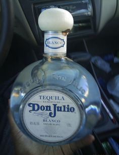 a person holding a bottle of tequila in their hand next to the steering wheel of a car