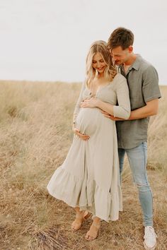 a pregnant couple cuddles while standing in the middle of a field with tall grass