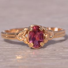 This Stunning Piece, Known As The Rosy Tourmaline, Features A Captivating Oval-Cut Tourmaline At Its Center, Exuding A Vibrant Rosy Hue. The Tourmaline Is Elegantly Set In A 14 Karat Yellow Gold Band With Intricate Detailing That Enhances Its Classic Beauty. This Exquisite Ring Is Currently A Finger Size 4.25 Yet Can Be Adjusted To Any Finger Size For An Additional Charge Upon Request, Ensuring A Perfect Fit. Yellow Gold Color, Tourmaline Ring, Classic Beauty, Gold Band, Womens Jewelry Rings, Gold Bands, Oval Cut, Red Yellow, Lady In Red