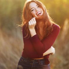 a woman with red hair is laughing and posing for the camera while standing in tall grass