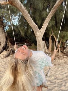 a woman laying on a swing in the sand near a tree with no leaves or branches