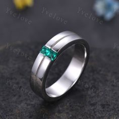 a white gold ring with a green emerald stone in the center on a black surface