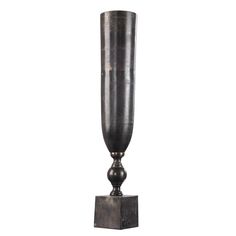 a tall metal vase sitting on top of a wooden block in front of a white background