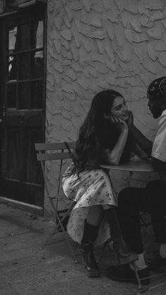 black and white photograph of two people sitting on a bench talking to each other outside