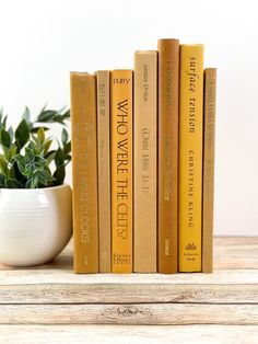 three yellow books are sitting on a shelf next to a potted plant and a white vase