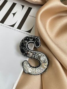 a brooch that is laying on top of a satin material sheet with the letter s in it