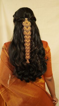 the back of a woman's head with long hair and gold jewelry on it